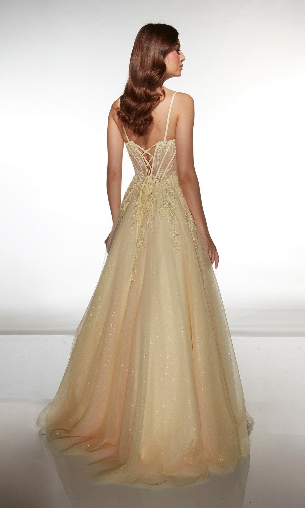 A woman faces away, wearing the Alyce 62061: a floor-length, light yellow sleeveless prom dress with a tulle ballgown skirt, lace-up back, thin straps, and subtle glitter accents.